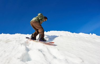 Erkek snowboardcu, güneşli kış gününde açık mavi gökyüzünün fotokopi alanı üzerinde dağdan aşağı derin kar altında snowboard yapıyor.