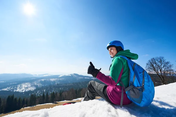 Snowboarder Młoda Kobieta Kasku Plecakiem Siedzi Śniegu Regulacji Snowboardu Tle — Zdjęcie stockowe