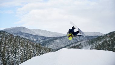 Snowboardcudan gelen muhteşem bir serbest uçuş görüntüsü. Bulutlu gökyüzüne ve arka planda nefes kesen dağlara karşı yamaçta güzel bir snowboard atlayışı. Uzayı kopyala Ekstrem spor konsepti