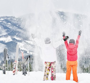 Arka planda büyüleyici manzaralara karşı karda oynayan genç turistlerin arka plan görüntüsü. Beyaz kar üzerinde canlı renkli takım elbiseler. Unutulmaz anlar. Kış sporları anlayışı, eğlence