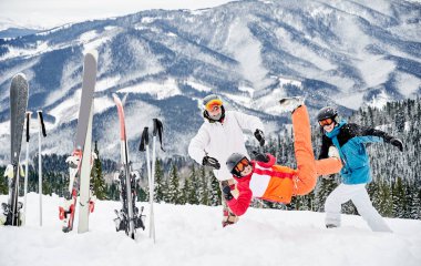 Canlı kış sporları takımları giymiş bir grup arkadaş dağlarda kar altında eğleniyorlar. Kayak direkleri ve kayaklar karda sıkıştı, neşeli insanlar güzel dağlara karşı kar oynuyor..