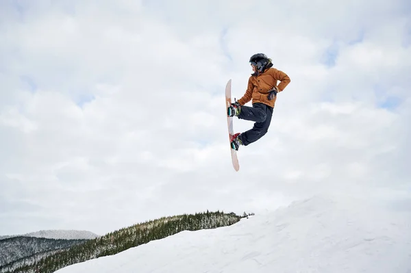 冬のジャケットとヘルメットの男のスノーボーダーは 空気中をジャンプします 冬の山の中で雪の丘を滑り降りながら 立派な子供がスノーボードでジャンプします 冬のスポーツ活動の概念 — ストック写真