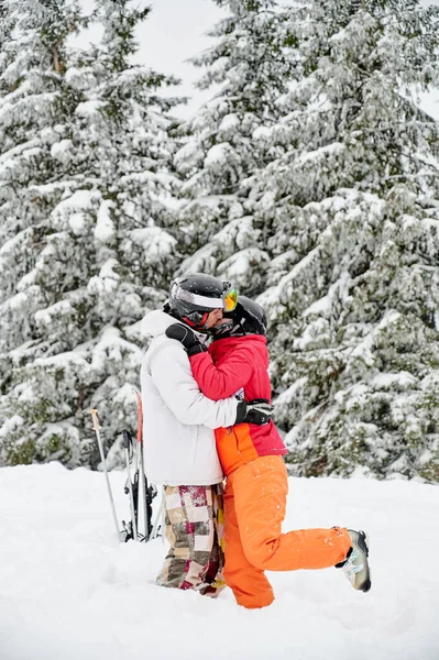 若いカップルの観光客が背景に魅力的な雪のスプルースの森にキスをします 白い雪の上に鮮やかなカラフルなスーツ スキーと関係の概念 — ストック写真