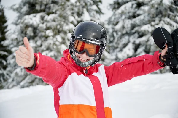 年轻女子穿着滑雪冬季夹克 头戴头盔 看着相机 面带微笑 穿着滑雪护目镜的快乐的女滑雪者把双手伸向两边 并竖起大拇指 欢乐与冬季体育活动的概念 — 图库照片