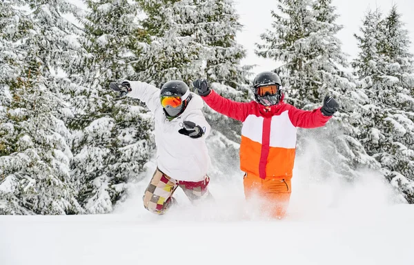 パウダースノーを駆け抜け手を上げるスキージャケットやヘルメットのカップルは 雪の木を背景に冬の森の中で楽しい時間を過ごしています レジャー 楽しさと関係の概念 — ストック写真