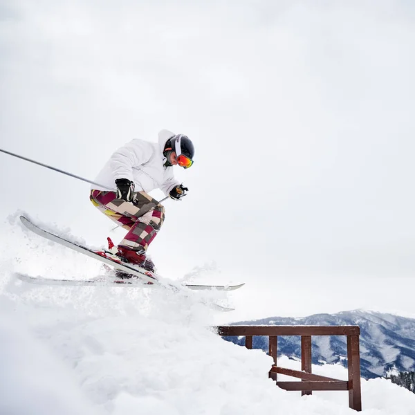 穿着白色冬季夹克的年轻人滑雪者侧视图滑落在雪地覆盖的斜坡上 滑雪板上有固定脚后跟的捆扎 穿着滑雪服 头戴钢盔 在山中新雪上滑行的人 — 图库照片