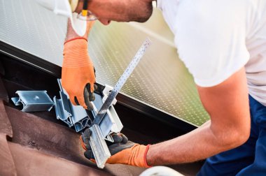 Fotovoltaik etkilerle elektrik üretmek için evin çatısına güneş paneli inşa eden işçiler. Montaj ekipmanlarını ölçmek için cetvel kullanan adamı kapat.