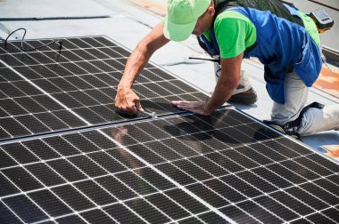 Evin çatısında fotovoltaik güneş paneli inşa eden bir işçi. Ingiliz anahtarının yardımıyla güneş modülü kuran insan mühendisi. Alternatif ve yenilenebilir enerji üretimi kavramı.