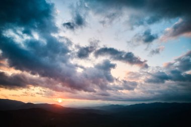 Ormanda hava manzarası nefes kesici gün batımı. Güneş ışınları dramatik bulutları delip geçiyor. Yuvarlanan tepeler ve vadiler boyunca altın parıltılar saçıyor. Uzak dağlar huzur ve resim manzarası yaratıyor..