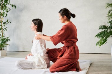 Masör Tayland yogası masajı yapıyor. Kadın terapist, kadın hasta için evde geleneksel masaj tedavisi uyguluyor. Müşteri mindere oturuyor, meditasyon yapıyor, sakin bir atmosferde el masajının keyfini çıkarıyor..