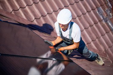 Evin çatısına güneş paneli inşa eden bir işçi. Dışarıda fotovoltaik güneş modülü kuran miğferdeki adam mühendis. Alternatif, yeşil ve yenilenebilir enerji üretimi kavramı.