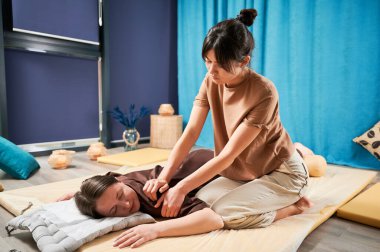 Masör Tayland yogası masajı yapıyor. Kadın terapist, kadın hasta için evde geleneksel masaj tedavisi uyguluyor. Müşteri paspasın üzerinde uzanıyor, meditasyon yapıyor, sakin bir atmosferde el masajının keyfini çıkarıyor..