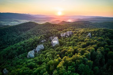 Nefes kesen günbatımı, engin ve sık ormanların üzerinde altın bir parıltı saçar, engebeli kaya oluşumları ağaçların arasından süzülür. Dovbush Kayaları, Karpat Dağları, Ukrayna.