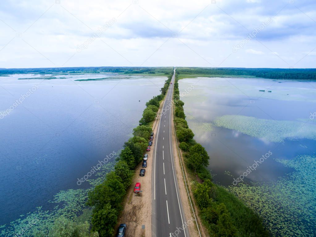 Landscape of an asphalt road. View from above on the road going along the blue river. Summer photography with bird's eye view.