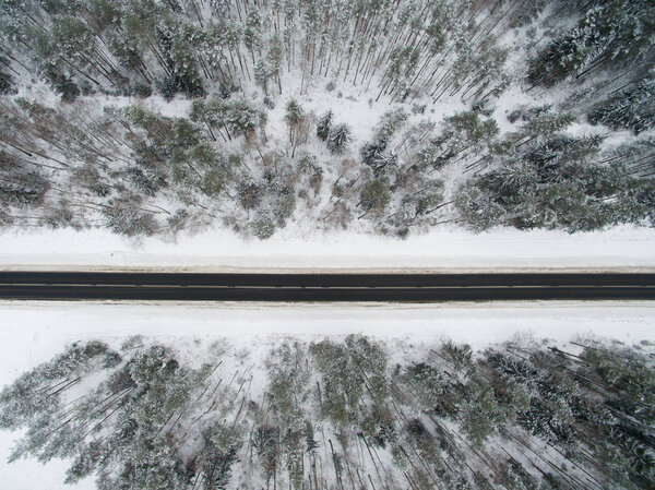 Winter forest and asphalt road. View from above. The photo was taken with a drone. Pine and spruce forest with a black road in the snow. — Stock Image Winter Forest Asphalt Road View Photo Taken Drone Pine Spruce — Stock Photo, Image