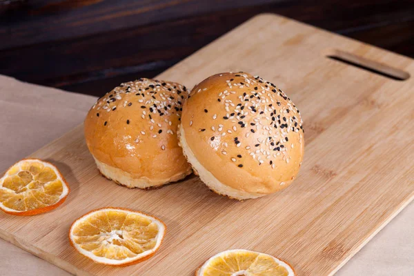 Heiße süße Brötchen auf rustikalem Hintergrund. geformte Nahrung mit Sesam auf Schneidebrett herum mit trockenen Orangen — Stockfoto