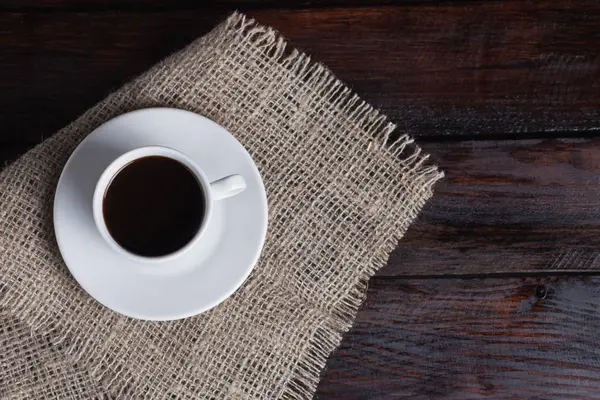 Xícara branca de café em tecido de linho no fundo escuro do vintage. Vista superior — Fotografia de Stock