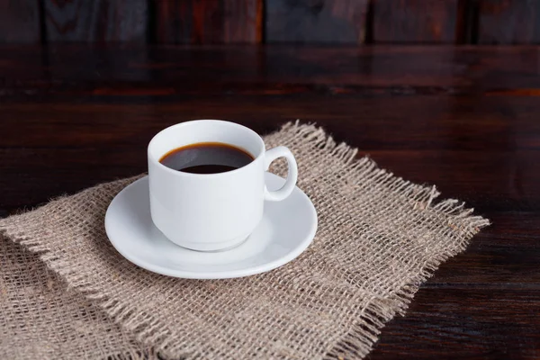 Weiße Tasse Kaffee auf Leinenstoff auf dunklem Vintage-Hintergrund — Stockfoto