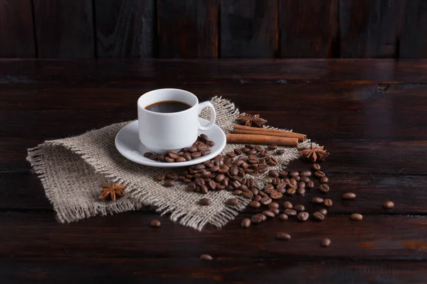 White cup of coffee with coffee grains near on linen fabric on the dark vintage background — Stock Photo, Image