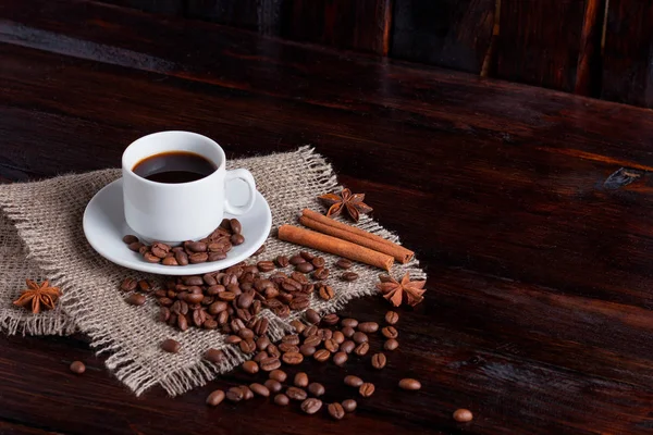 Ceașcă albă de cafea cu boabe de cafea lângă țesătura de in pe fundalul întunecat de epocă — Fotografie, imagine de stoc