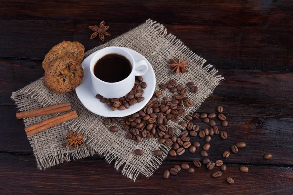 Weiße Tasse Kaffee mit Kaffeekörnern in der Nähe und Keksen auf Leinenstoff auf dunklem Vintage-Hintergrund — Stockfoto