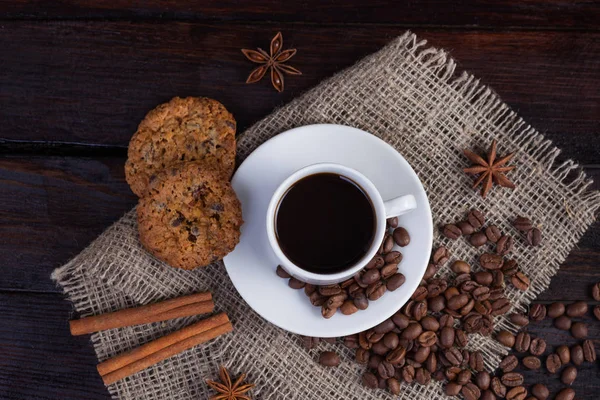 Weiße Tasse Kaffee mit Kaffeekörnern in der Nähe und Keksen auf Leinenstoff auf dunklem Vintage-Hintergrund — Stockfoto