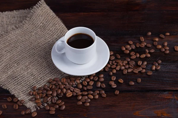 Xícara branca de café com grãos de café perto de tecido de linho no fundo escuro do vintage — Fotografia de Stock