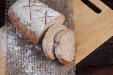 Keten kumaş parçası ile ahşap arka plan üzerinde dağınık un ile bir meşe panosuna dilimlenmiş adet taze kahverengi ekmek