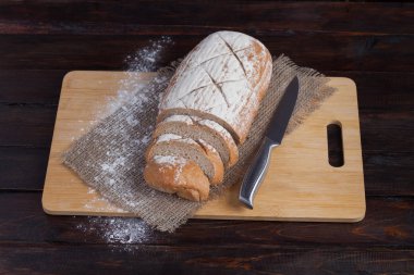 Taze kahverengi ekmek dilimlenmiş adet meşe panosunda bir ahşap zemin üzerine dağınık un ile çelik bir bıçak ile keten kumaş ile. Fotoğraf Üstten Görünüm