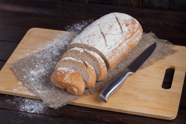 Taze kahverengi ekmek dilimlenmiş adet meşe panosunda bir ahşap zemin üzerine dağınık un ile çelik bir bıçak ile keten kumaş ile. Fotoğraf Üstten Görünüm