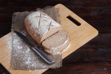 Taze kahverengi ekmek dilimlenmiş adet meşe panosunda bir ahşap zemin üzerine dağınık un ile çelik bir bıçak ile keten kumaş ile. Fotoğraf Üstten Görünüm