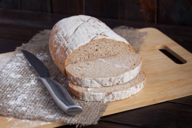 Taze kahverengi ekmek dilimlenmiş adet meşe panosunda bir ahşap zemin üzerine dağınık un ile çelik bir bıçak ile keten kumaş ile. Fotoğraf Üstten Görünüm