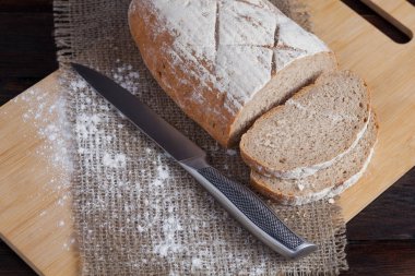 Taze kahverengi ekmek dilimlenmiş adet meşe panosunda bir ahşap zemin üzerine dağınık un ile çelik bir bıçak ile keten kumaş ile. Fotoğraf Üstten Görünüm