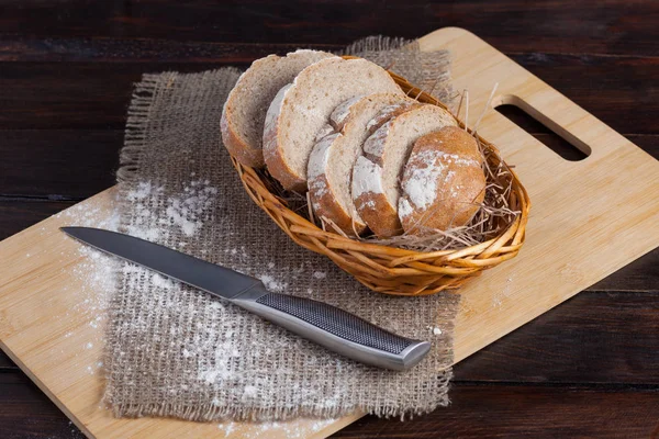 Roti coklat segar dengan potongan-potongan yang diiris di papan ek dengan tepung yang tersebar di latar belakang kayu dengan kain linen dengan pisau baja. Tampilan puncak foto — Stok Foto