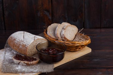 Taze bir hasır kase meşe panosunda bir ahşap zemin üzerine dağınık un ile bir kase lezzetli bir reçel yanında keten kumaş parçaları ekmek dilimlenmiş