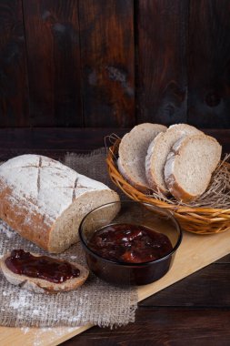 Taze bir hasır kase meşe panosunda bir ahşap zemin üzerine dağınık un ile bir kase lezzetli bir reçel yanında keten kumaş parçaları ekmek dilimlenmiş