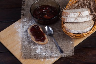 Taze bir hasır kase meşe panosunda bir ahşap zemin üzerine dağınık un yanında bir kase lezzetli bir reçel ve bir kaşık keten kumaş parçaları ekmek dilimlenmiş