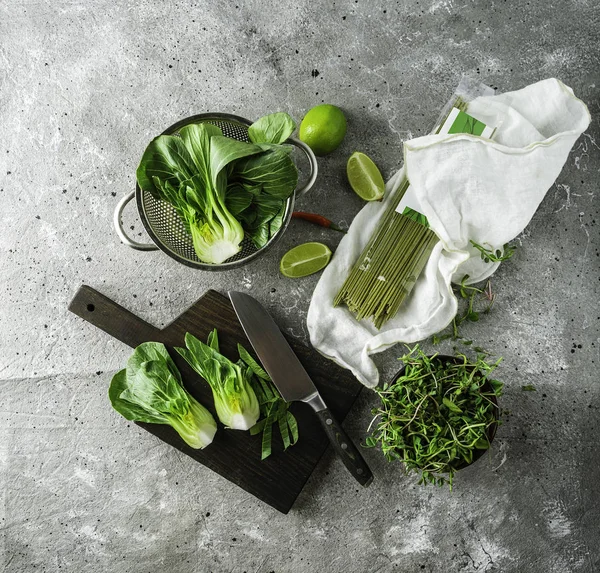 Bebé bok choi mitades, fideos de té verde sin cocer, limas, brotes verdes sobre fondo gris. Vista superior, imagen cuadrada — Foto de stock gratis