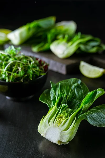 Baby bok choi jumătăți, limes, germeni verzi pe fundal negru — Fotografie, imagine de stoc