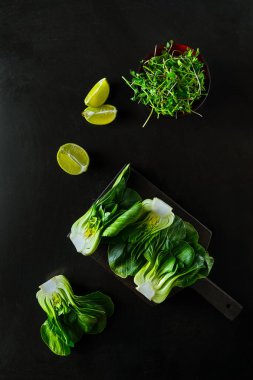 Bebek bok Choi yarısı, kireç dilimleri, siyah arka planda yeşil lahanası. Üstteki görünüm, dikey oryantasyon
