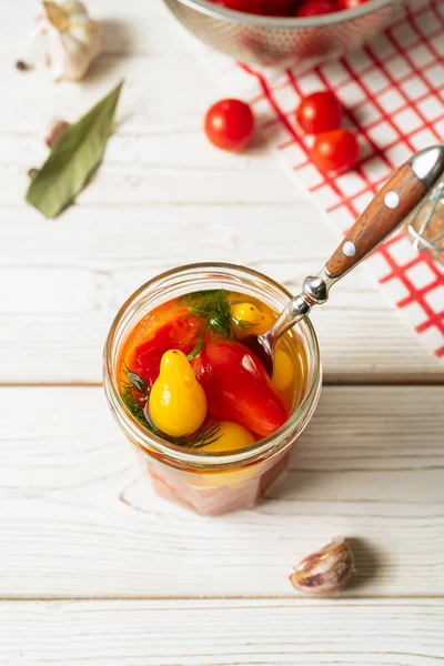 Marinated tomatoes in open glass jar, fork, cooking ingredients on white background. Horizontal image, top view. — Free Stock Photo