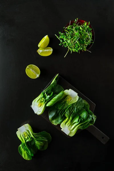 Bébé bok choi moitiés, quartiers de lime, choux verts sur fond noir. Vue de dessus, orientation verticale — Photo