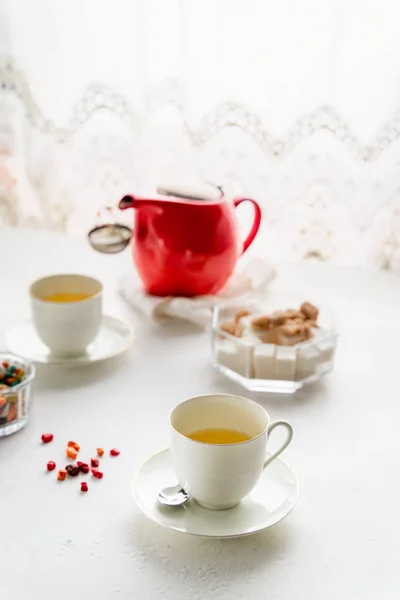 Panci teh merah, dua cangkir teh putih, mangkuk gula di atas meja oleh jendela — Stok Foto