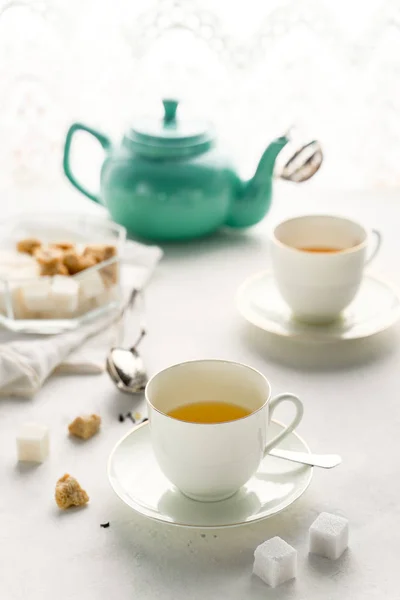Teko teh berwarna, dua cangkir teh putih, mangkuk gula di atas meja dengan jendela — Stok Foto
