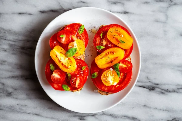 Öppen tomat smörgås på vit plåt på naturlig marmor bakgrund. Övre vy, horisontell orientering. — Stockfoto