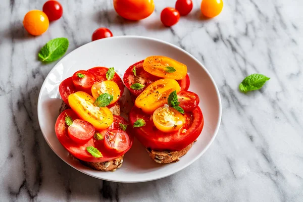 Öppen tomat smörgås på vit plåt på naturlig marmor bakgrund. Övre vy, horisontell orientering. — Stockfoto