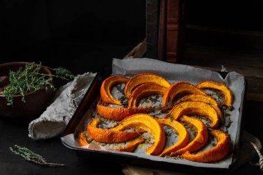 Fırın tepsisinde pişmiş dilimlenmiş kabak parçaları, koyu zemin üzerinde taze kekik.