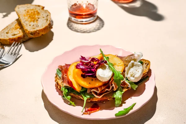 Parma jamón, mozzarella y melocotones sándwich en un plato, un poco de pan y vino de rosas tiro con luz dura, vista de cerca — Foto de Stock