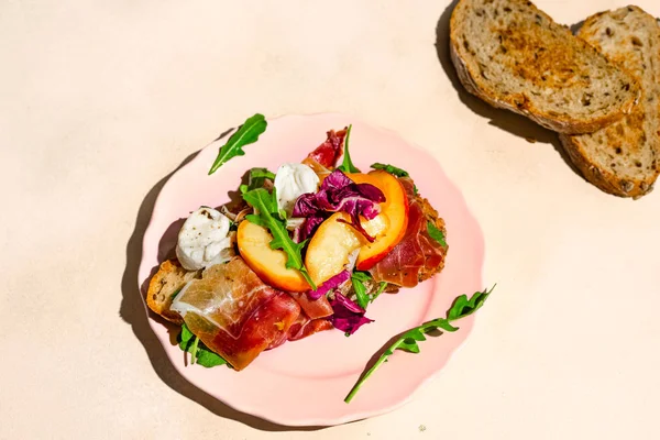 Närbild av Parma skinka, mozzarella och persikor smörgås på en tallrik, två bitar bröd, sköt med hårt ljus — Gratis stockfoto