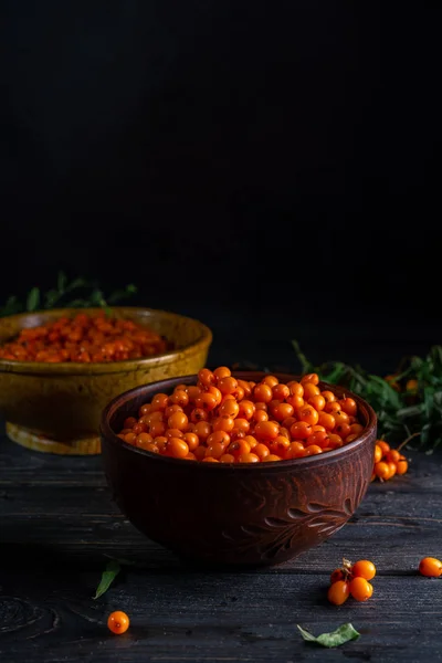 Bär och grenar av havtorn, skålar med bär på en mörk träbakgrund — Stockfoto